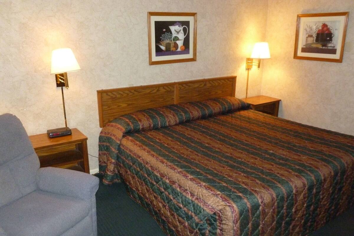 A hotel room with a bed, a chair, two nightstands with lamps, and two framed pictures on the wall.