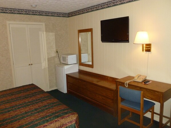 A hotel room with a bed, a desk with a chair, a telephone, a microwave, and a television on the wall.