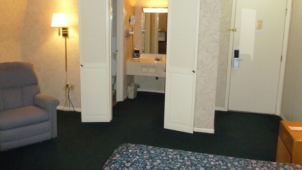 Une chambre d’hôtel avec un lit, une chaise, un bureau avec un miroir, un lavabo et une porte.
