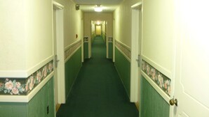 Un long couloir étroit, doté d’une moquette verte et de murs de couleur crème, qui mène à plusieurs portes au bout.