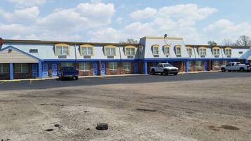 A motel with a row of rooms, a parking lot, and a dirt area in front.
