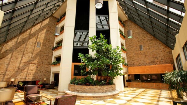 A spacious lobby with a high ceiling, a central planter with greenery, and a checkered floor pattern.
