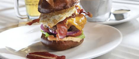 A burger with bacon, cheese, and lettuce on a white plate.