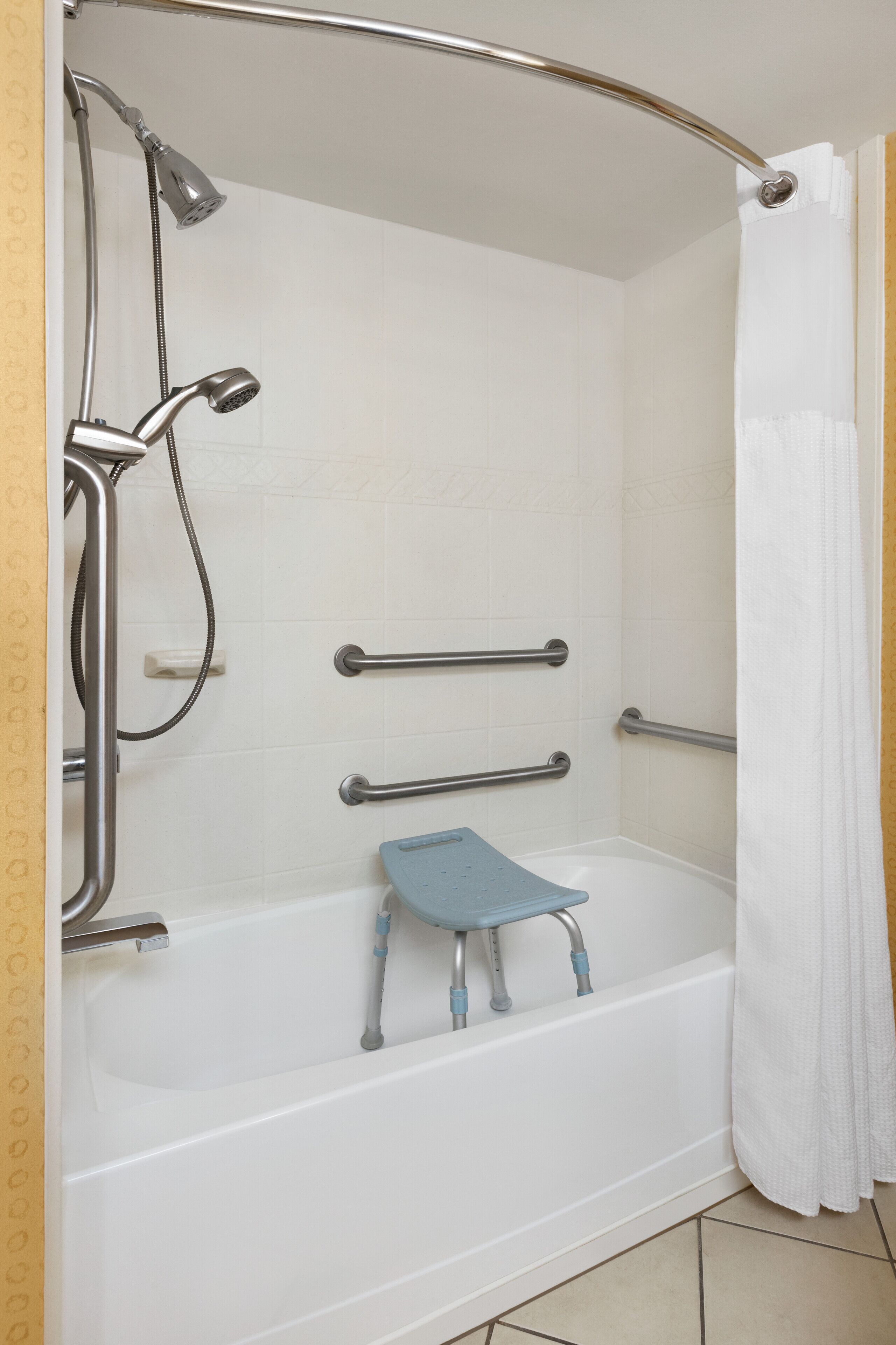 Une salle de bain équipée d’une douche, de barres d’appui et d’un banc accessible aux personnes en fauteuil roulant.