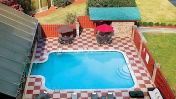 Una piscina con suelo de ajedrez, rodeada por una cerca roja, y con mobiliario exterior y sombrillas.