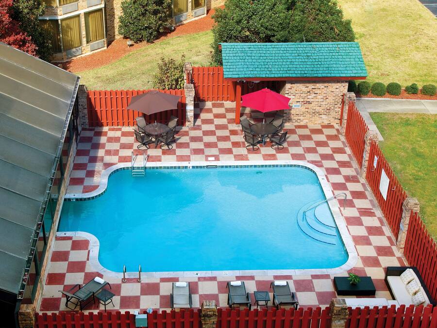 Una piscina con suelo de ajedrez, rodeada por una cerca roja, y con mobiliario exterior y sombrillas.