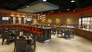 A modern restaurant with a bar area, multiple seating arrangements, and a television displaying a news program.