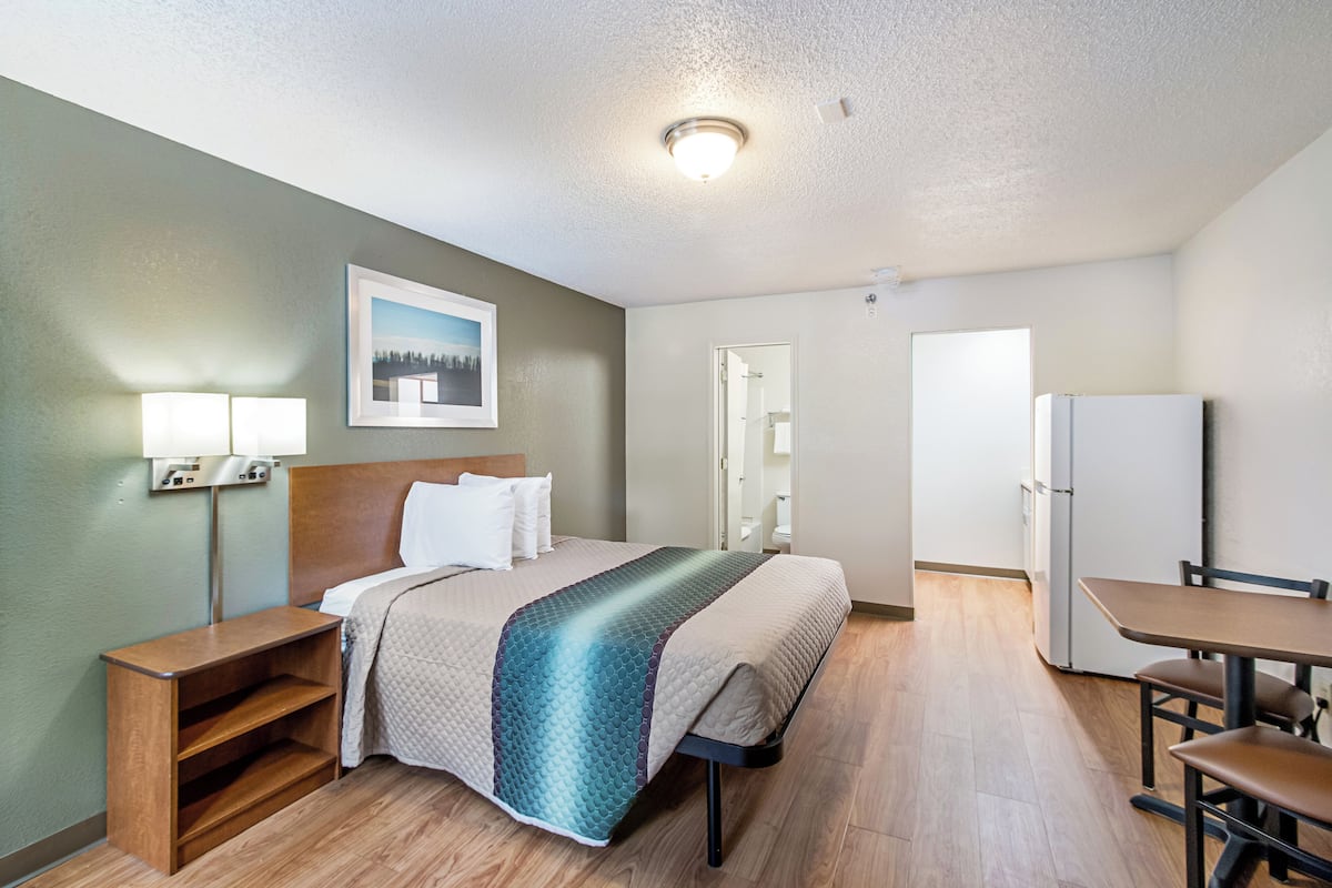 Quarto de hotel com cama, mesa de cabeceira, abajur e escrivaninha com cadeiras.
