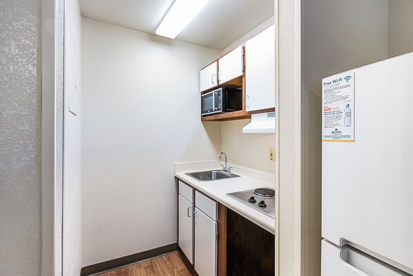 A compact kitchen with a microwave, sink, and stove, featuring white cabinetry and a white refrigerator.