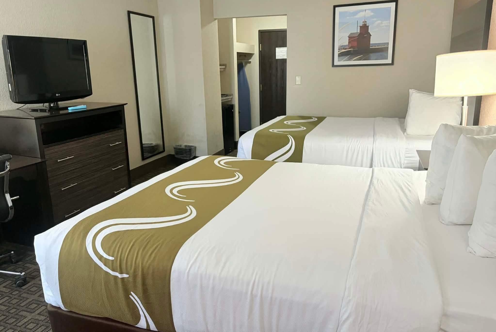 A hotel room with two beds, a TV, a desk, and a mirror.