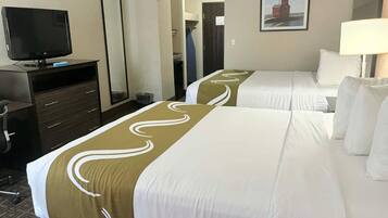 A hotel room with two beds, a TV, a desk, and a mirror.