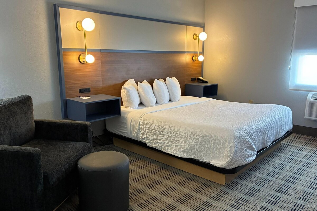 A hotel room with a large bed, two bedside tables with lamps, a chair, and a small ottoman.