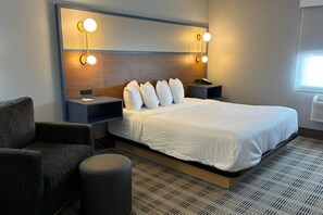 Une chambre d’hôtel avec un grand lit, deux tables de chevet avec des lampes, une chaise et un petit pouf.