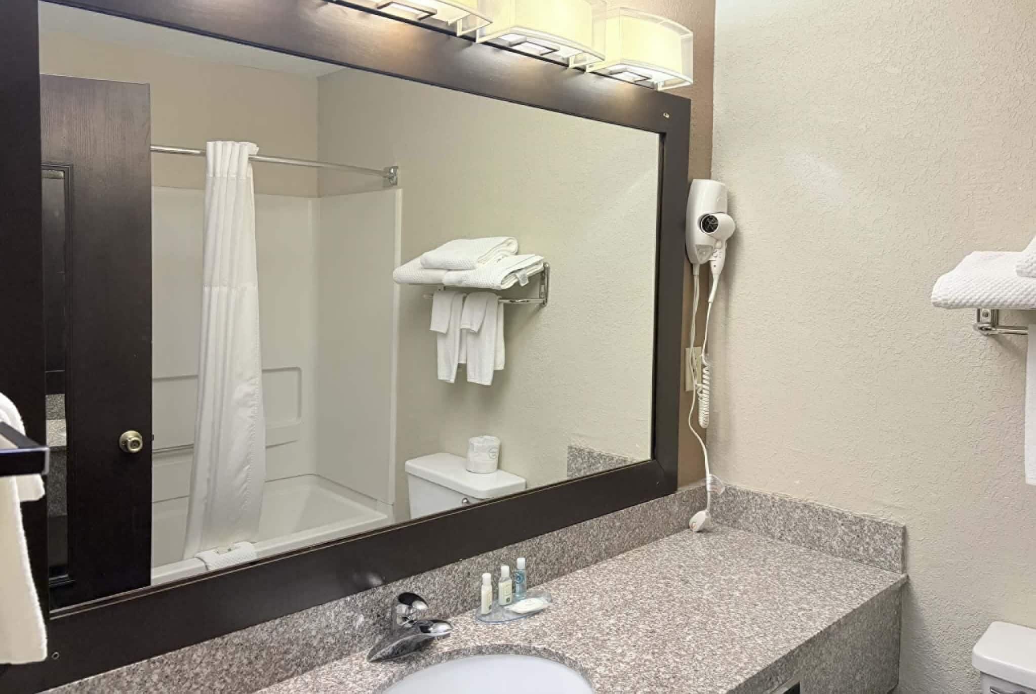 A hotel bathroom with a large mirror, a sink, a hairdryer, and a towel rack.