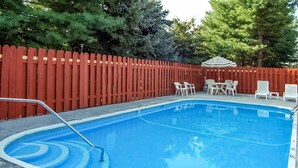A swimming pool with a red fence, white chairs, and a table with an umbrella.