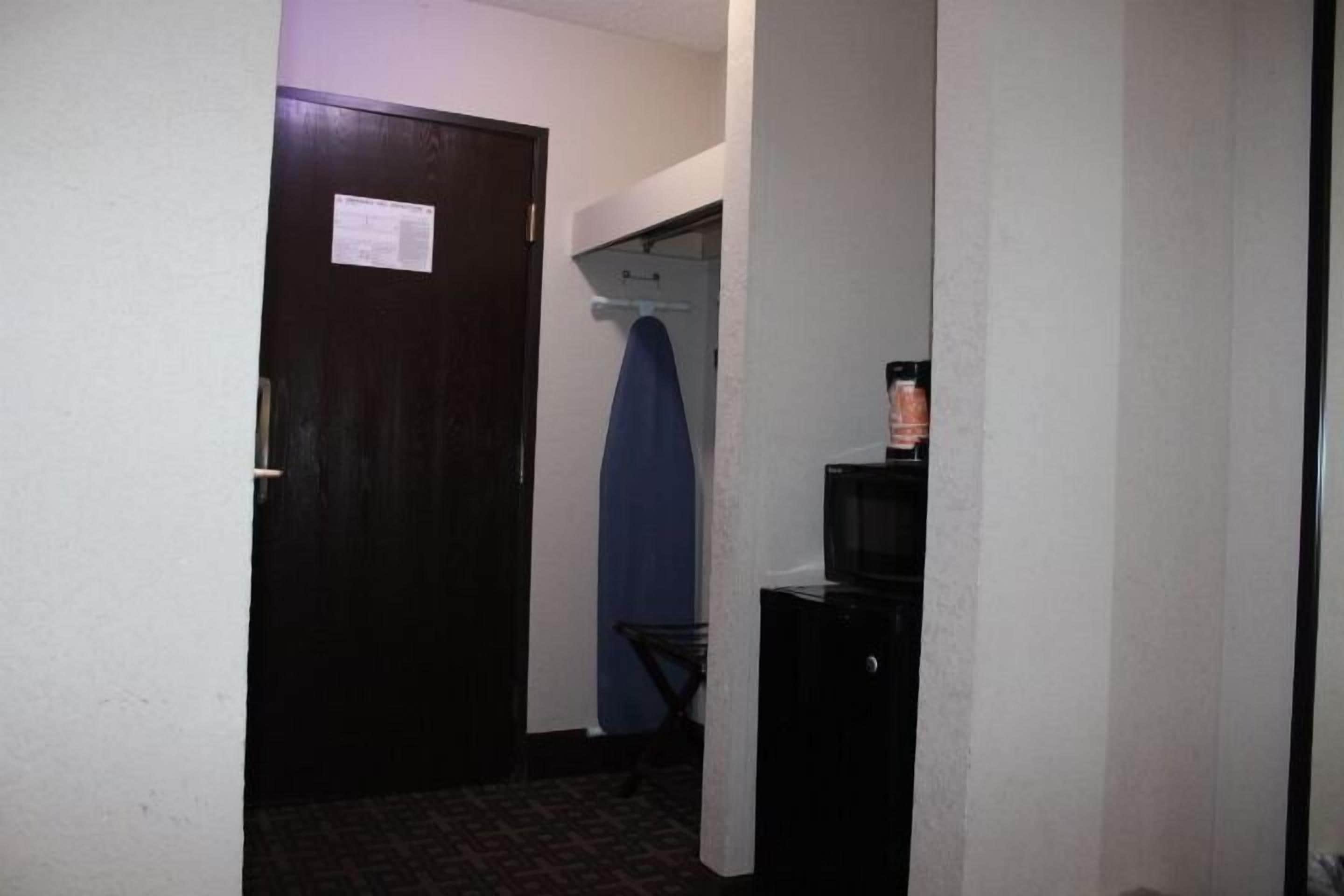 A narrow hallway with a dark door, a blue towel hanging on a rack, and a small black cabinet with a microwave on top.