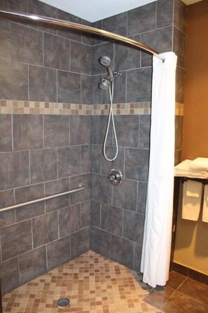 A shower with a curved glass door, a handrail, and a tiled floor. - AmericInn by Wyndham Holland MI (Holland)