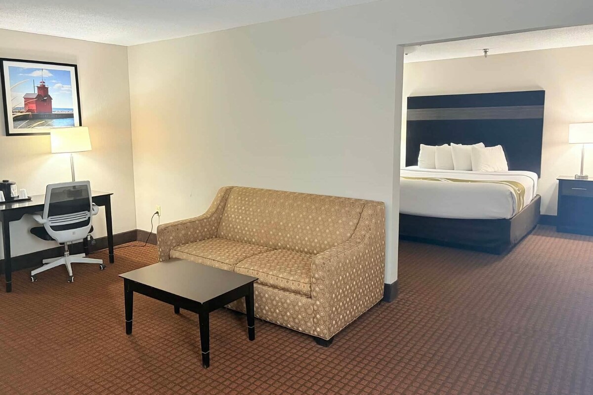 A hotel room with a bed, a sofa, a desk with a chair, and a lamp.