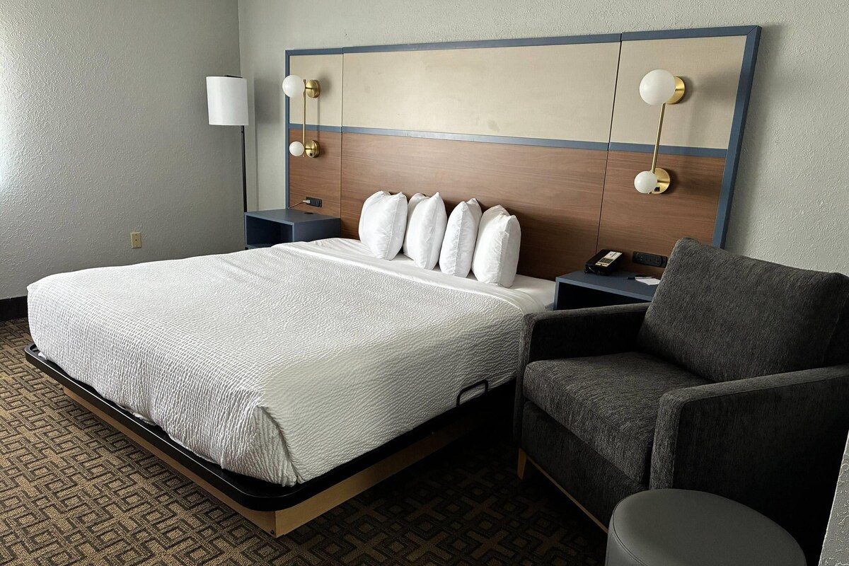 A hotel room with a large bed, a desk, a chair, and two bedside lamps.