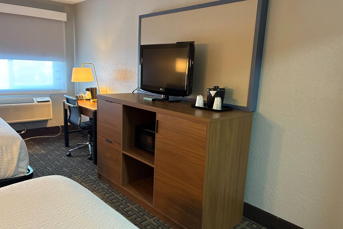 A hotel room with a bed, a desk with a lamp, a television, and a minibar.