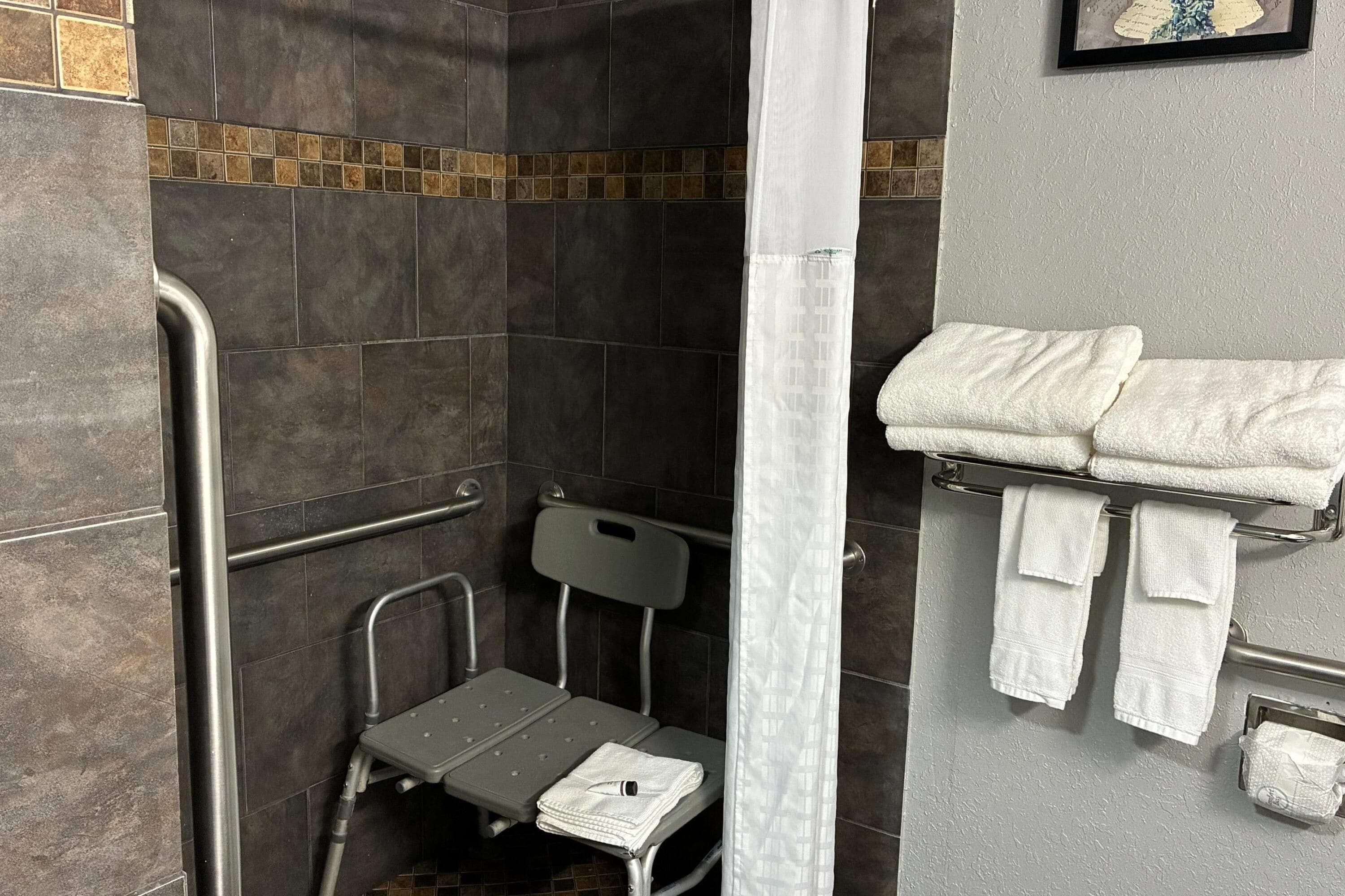 A shower area with a grab bar, a small step stool, and a towel rack with folded towels.