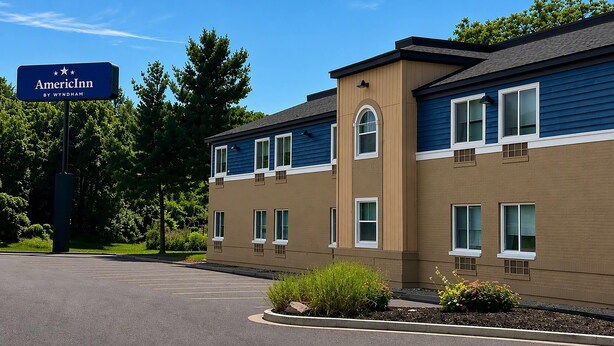 A two-story building with a blue and beige exterior, a parking lot, and a sign indicating it's an AmericInn by Wyndham hotel.