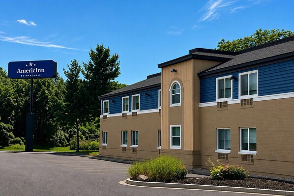 A two-story building with a blue and beige exterior, a parking lot, and a sign indicating it's an AmericInn by Wyndham hotel.