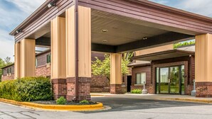 A hotel with a covered entrance, brick facade, and a landscaped area with bushes.