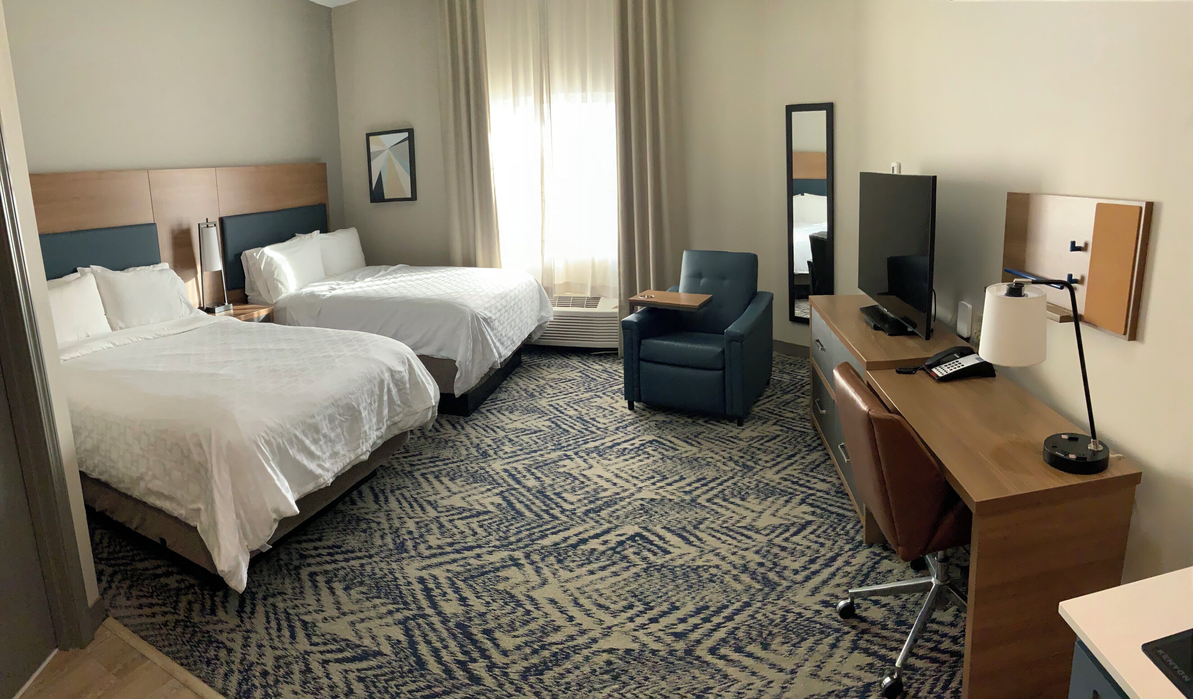 A hotel room with two beds, a desk with a computer, a chair, a TV, and a large window with curtains.