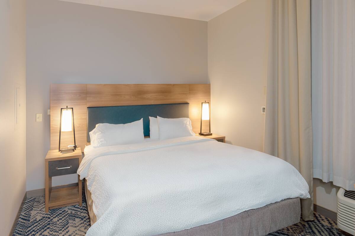 A neatly made bed with a wooden headboard, two bedside tables with lamps, and a patterned rug.