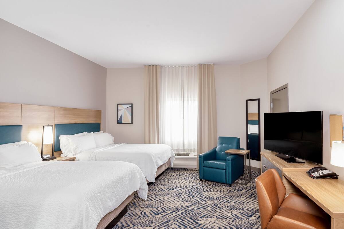 A hotel room with two beds, a TV, a desk, and a chair.