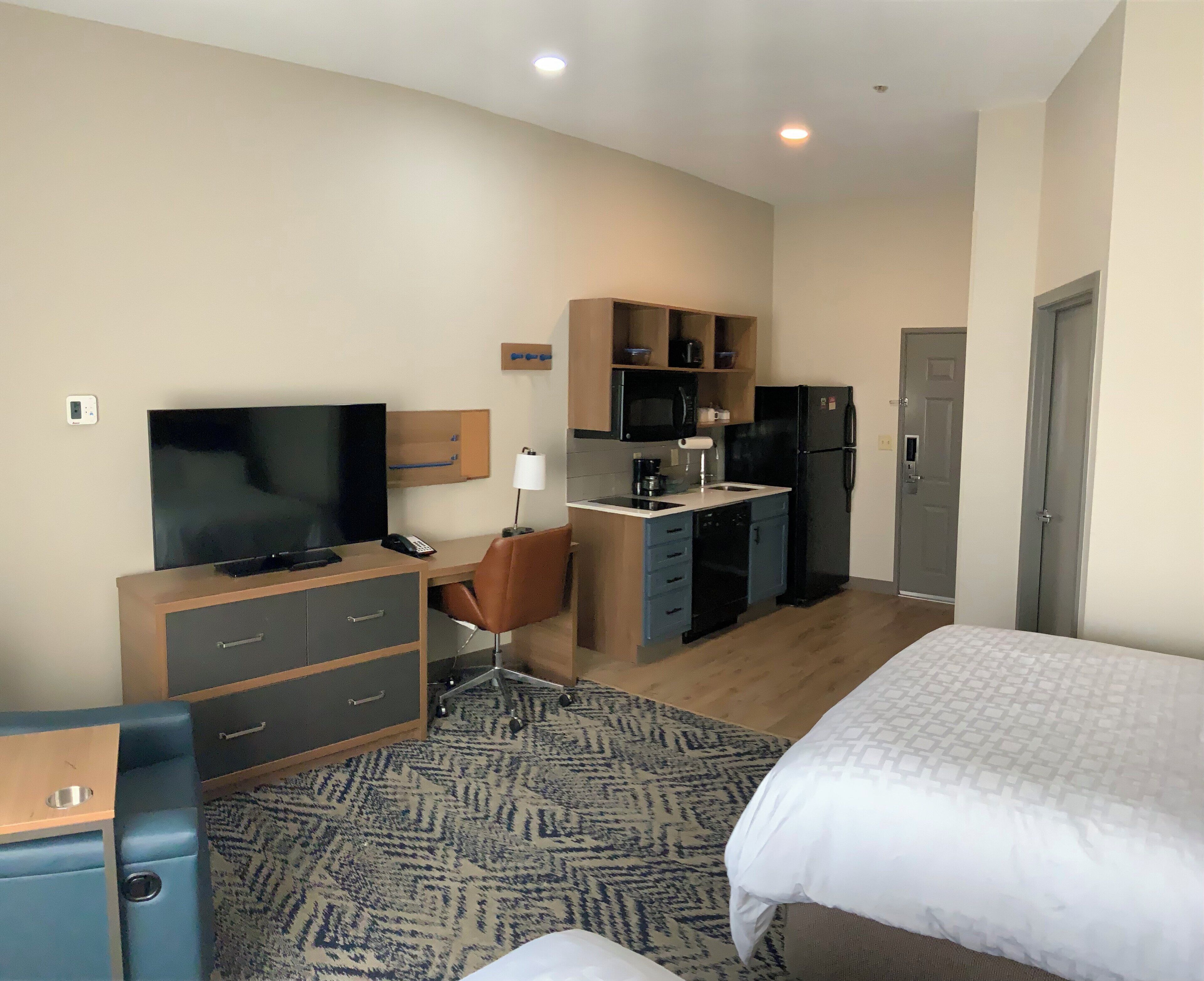 Une chambre d’hôtel équipée d’un lit, d’un bureau avec un ordinateur, d’une télévision, d’un four à micro-ondes et d’un réfrigérateur.