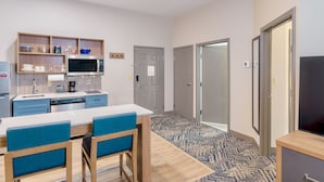 A modern kitchen with a microwave, coffee maker, and dishwasher. There is a dining table with blue chairs and a patterned rug.