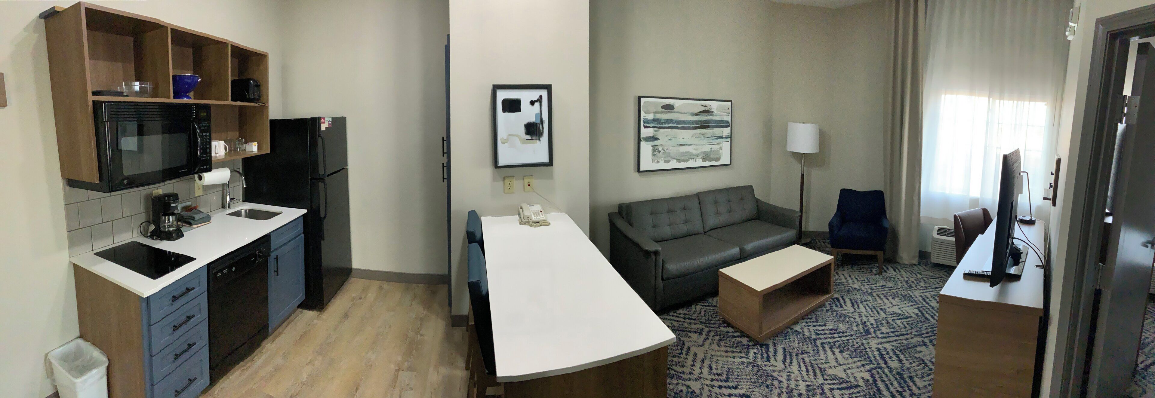 Una habitación de hotel compacta con kitchenette, un sofá, una mesita y una lámpara.