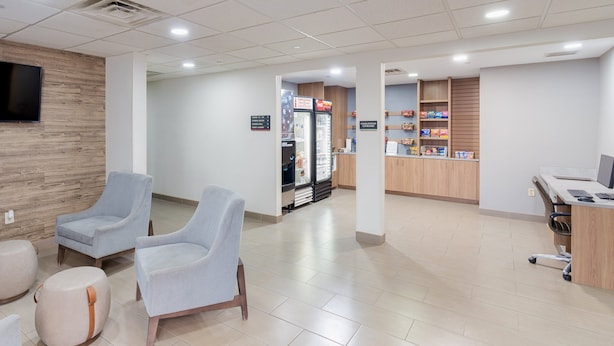 A modern interior with two light blue chairs, a wooden wall, a refrigerator, and a counter with snacks.