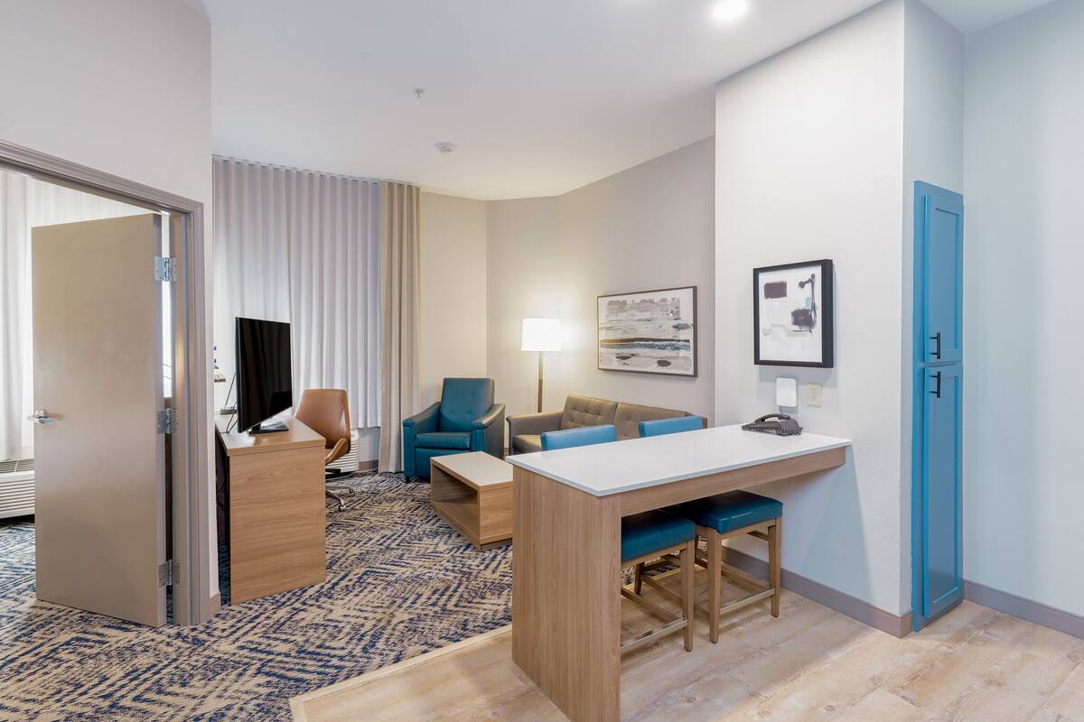 A hotel room with a desk, two chairs, a sofa, a lamp, and a painting on the wall.
