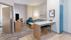 A hotel room with a desk, two chairs, a sofa, a lamp, and a painting on the wall.