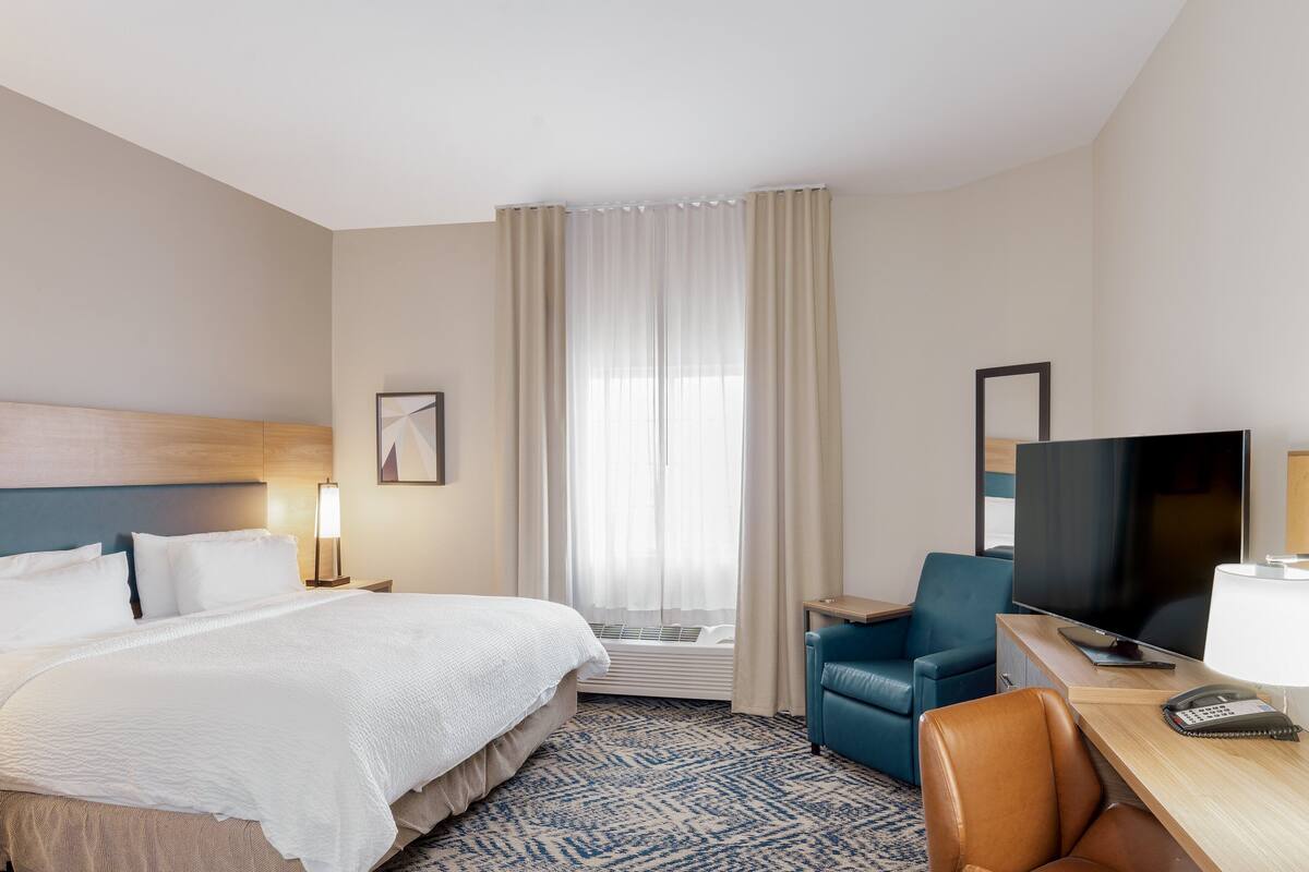 A hotel room with a bed, a desk with a TV, a chair, a lamp, and a telephone.