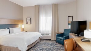 A hotel room with a bed, a desk with a TV, a chair, a lamp, and a telephone.