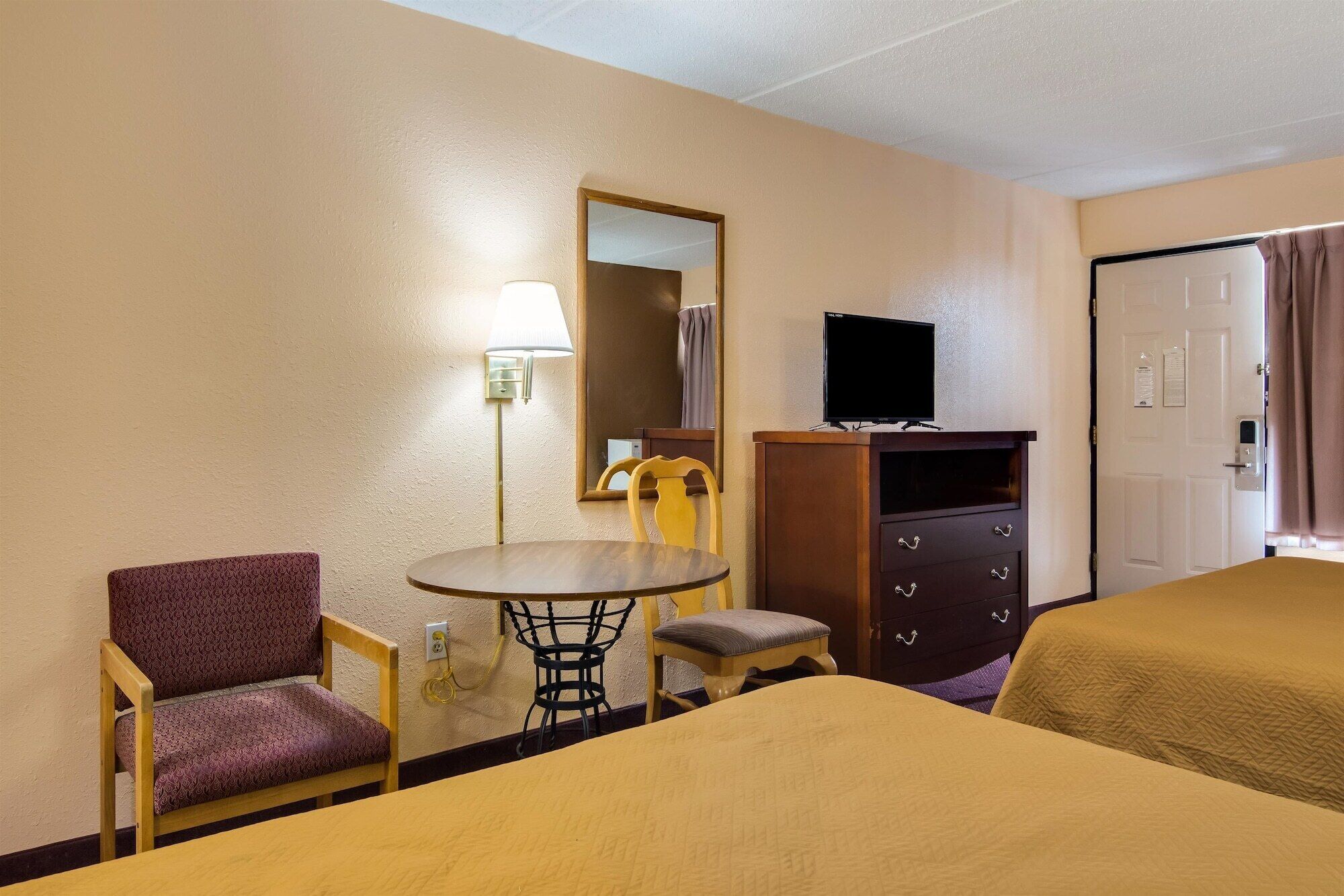 A hotel room with two beds, a desk with a chair, a TV, and a mirror.