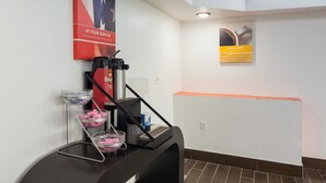 A coffee station with a Folgers coffee dispenser, a coffee machine, and a glass carafe. There are two baskets with pink tissues and a metal mesh container. - Motel 6 Macon, GA (Macon)