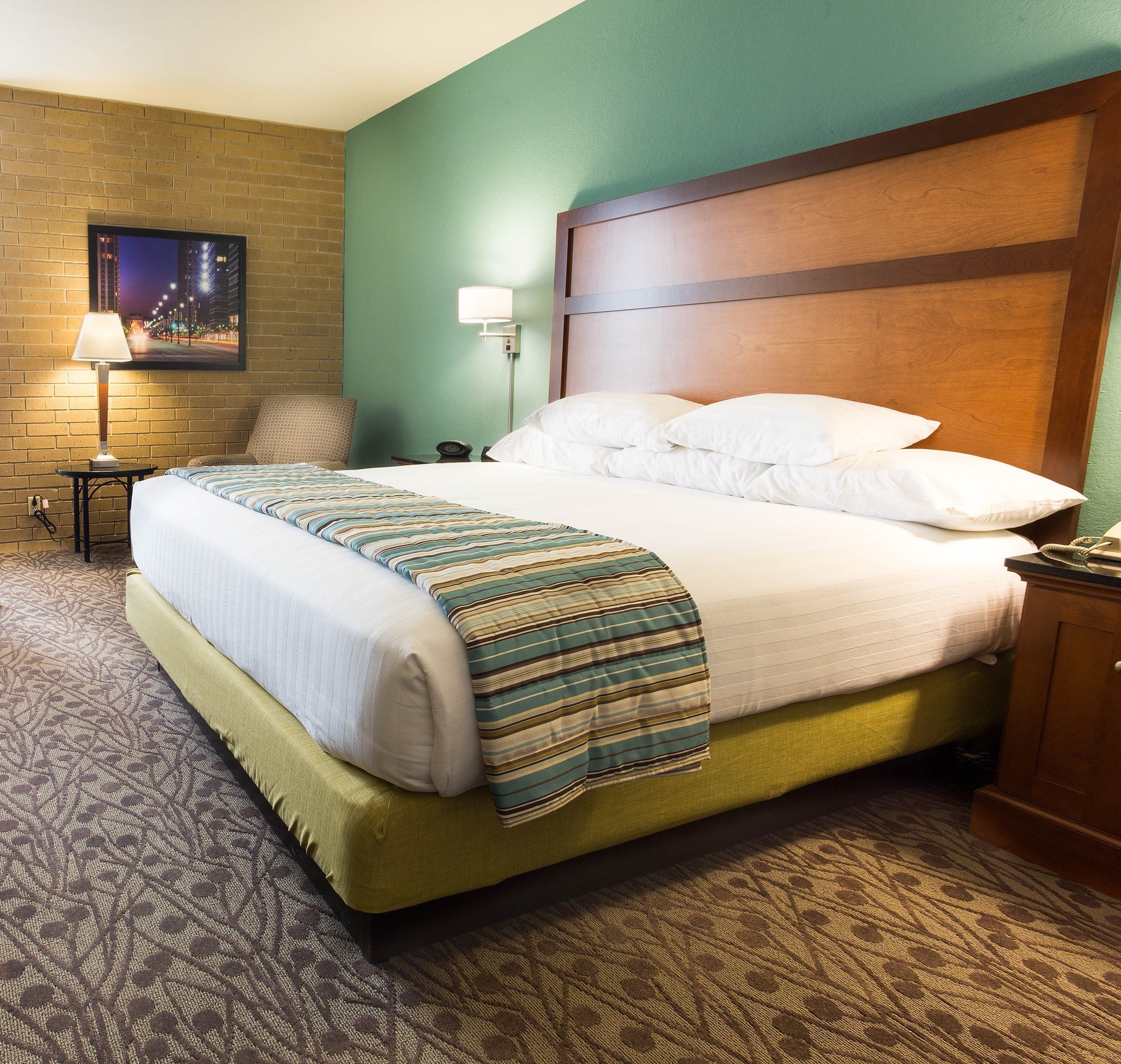 A hotel room with a large bed, a nightstand, a lamp, a chair, and a wall-mounted TV.