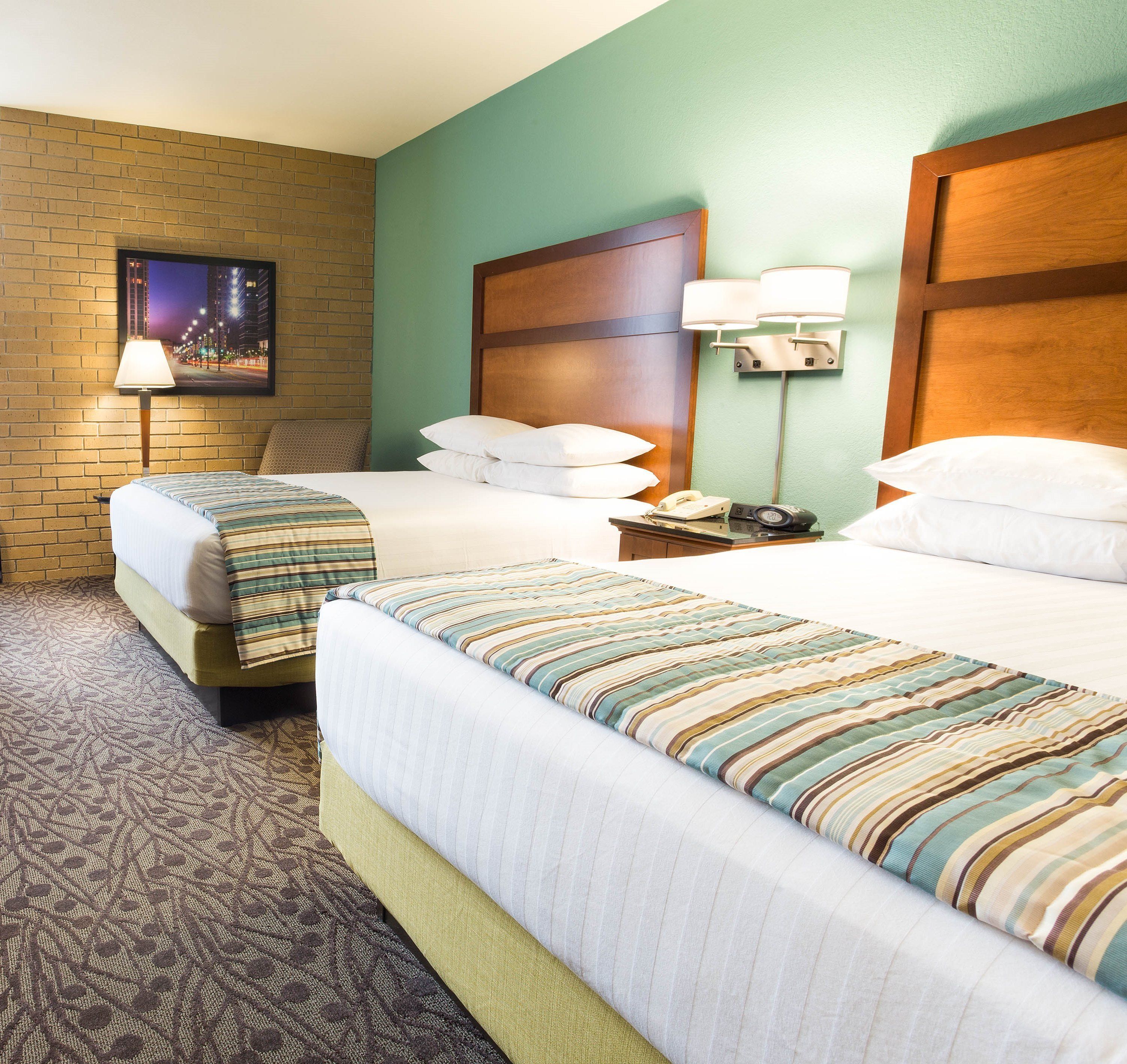 A hotel room with two beds, a brick wall, a painting, and a night view of a cityscape.