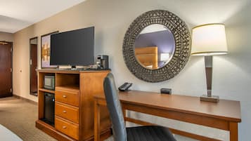 Une chambre d’hôtel équipée d’un bureau en bois, d’une télévision, d’un four à micro-ondes, d’une machine à café, d’un téléphone et d’un miroir.