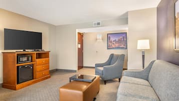 Habitación de hotel con televisión de pantalla plana, microondas, refrigerador pequeño, sofá, sillón y mesita de café.