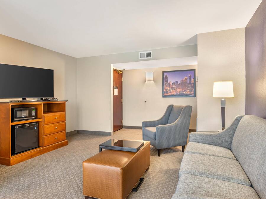 Habitación de hotel con televisión de pantalla plana, microondas, refrigerador pequeño, sofá, sillón y mesita de café.
