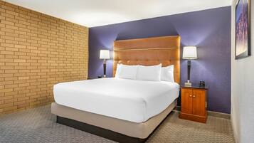 A hotel room with a large bed, two bedside tables with lamps, a wooden nightstand, and a brick wall.