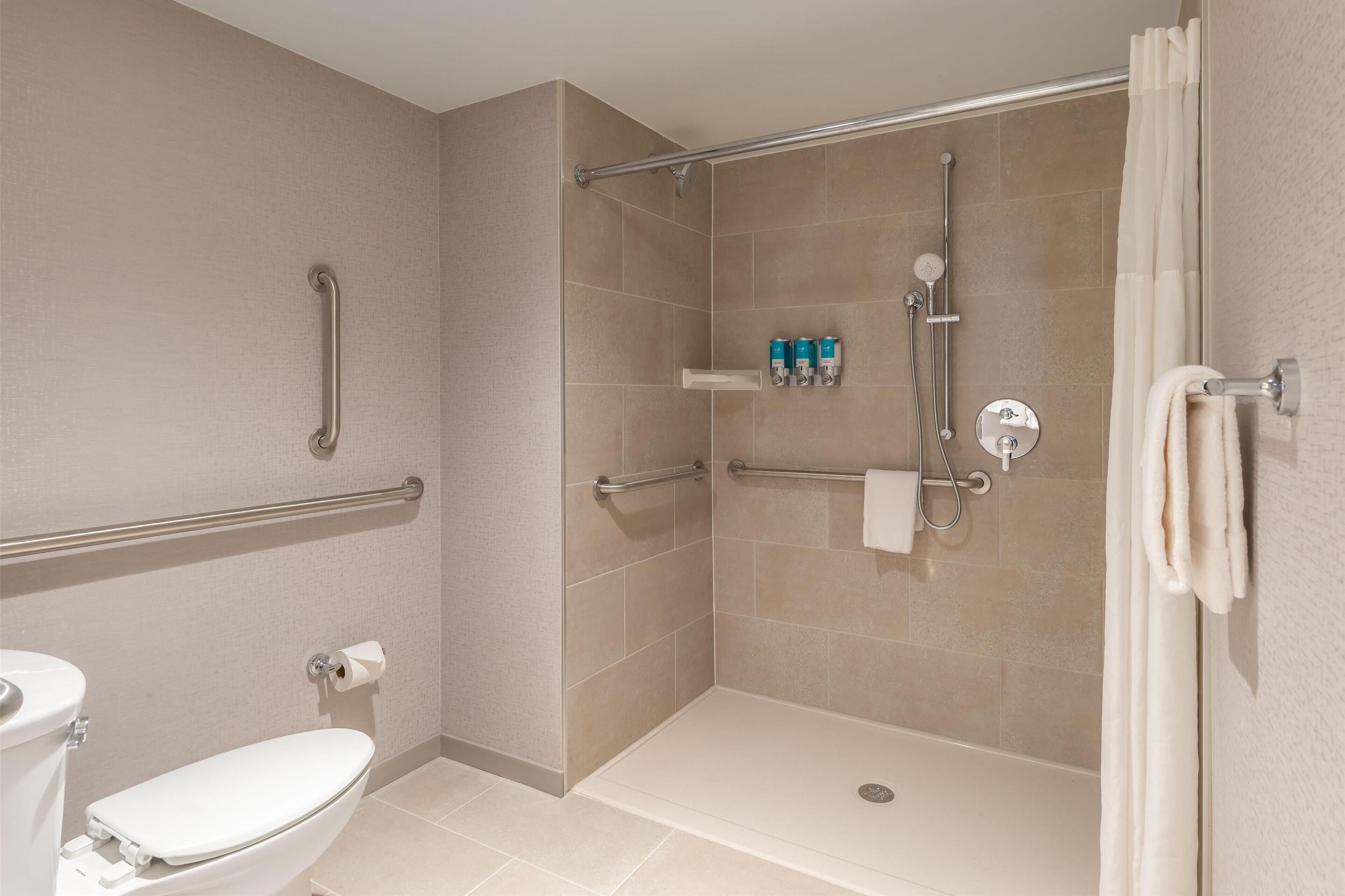 Un espace douche doté d’une porte en verre, de barres d’appui, d’un porte-serviettes et de toilettes.