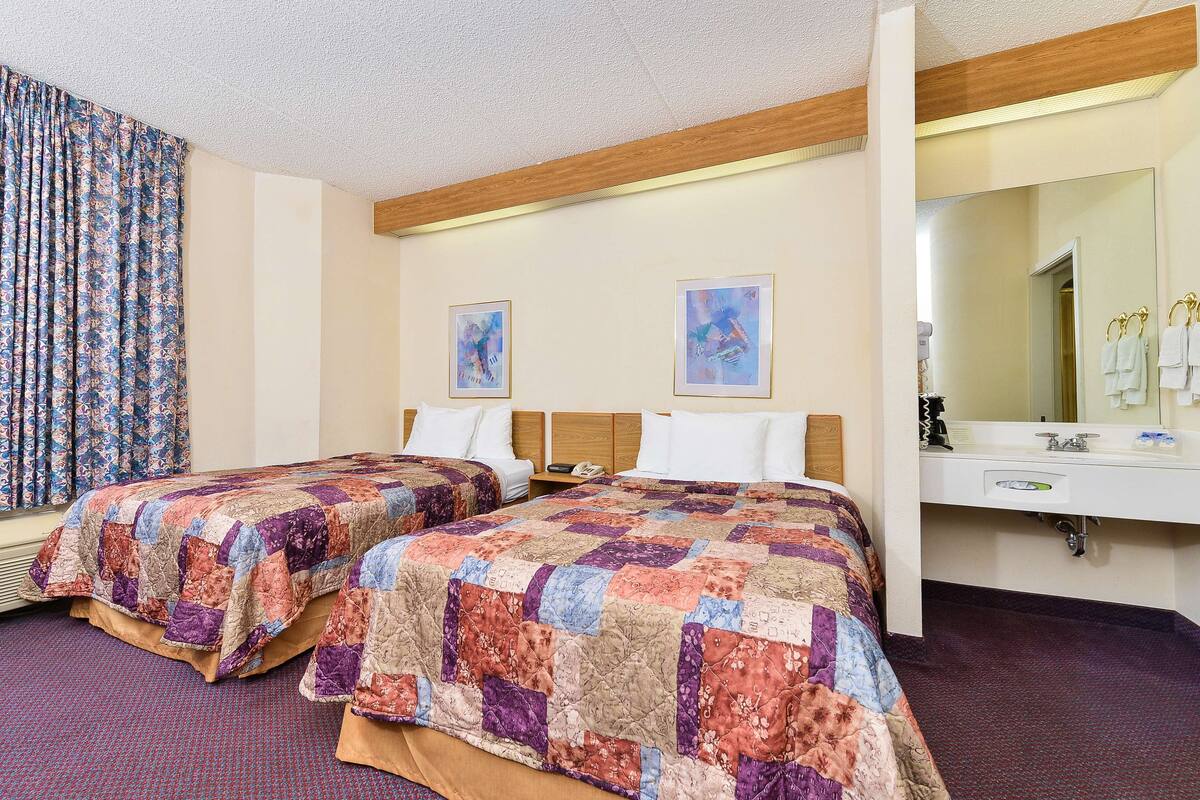 A hotel room with two beds, a large mirror, a sink, and artwork on the walls.