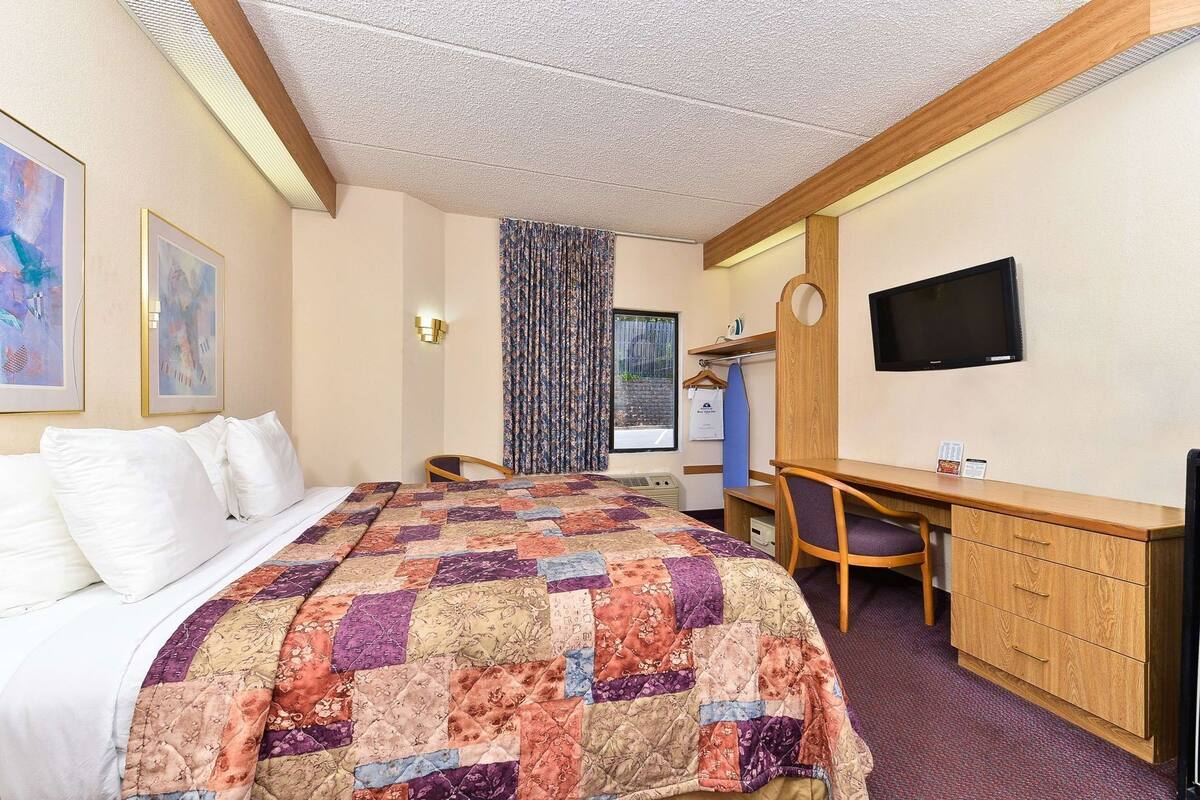A hotel room with a bed, a desk, a chair, a television, and a window with curtains.